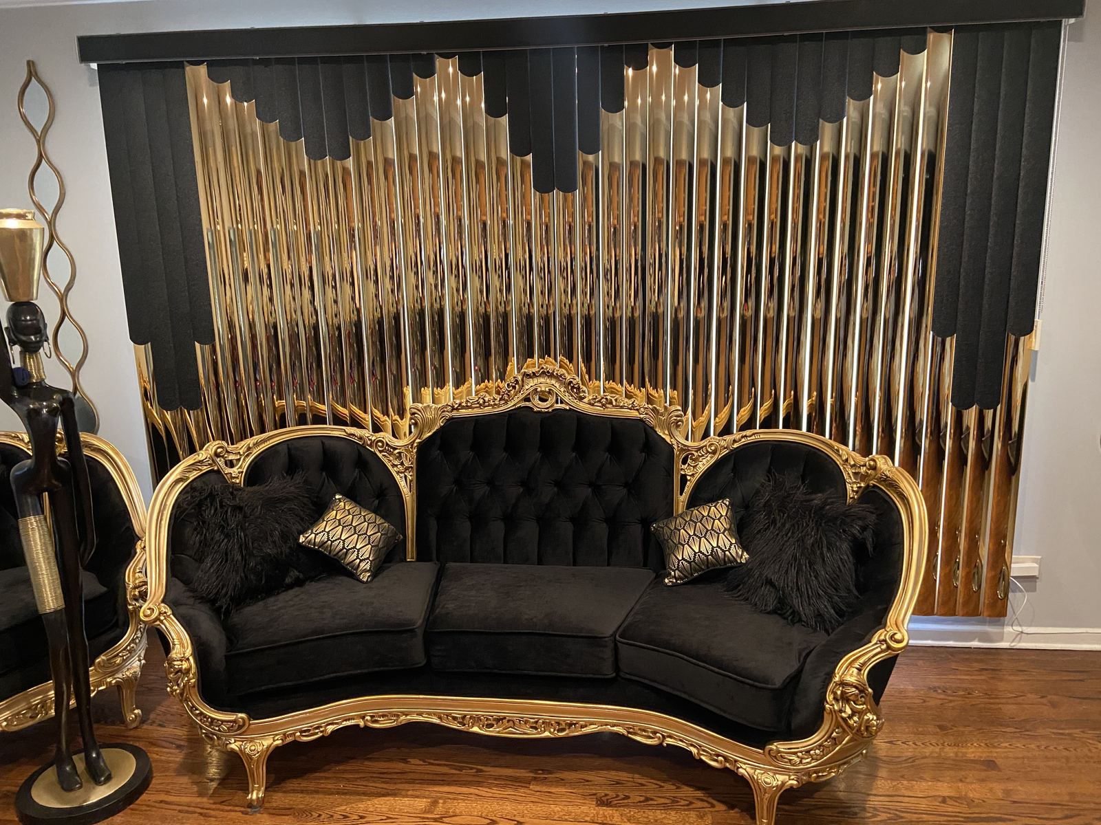 Black and gold custom vertical blinds with a scalloped valance behind a black and gold sofa